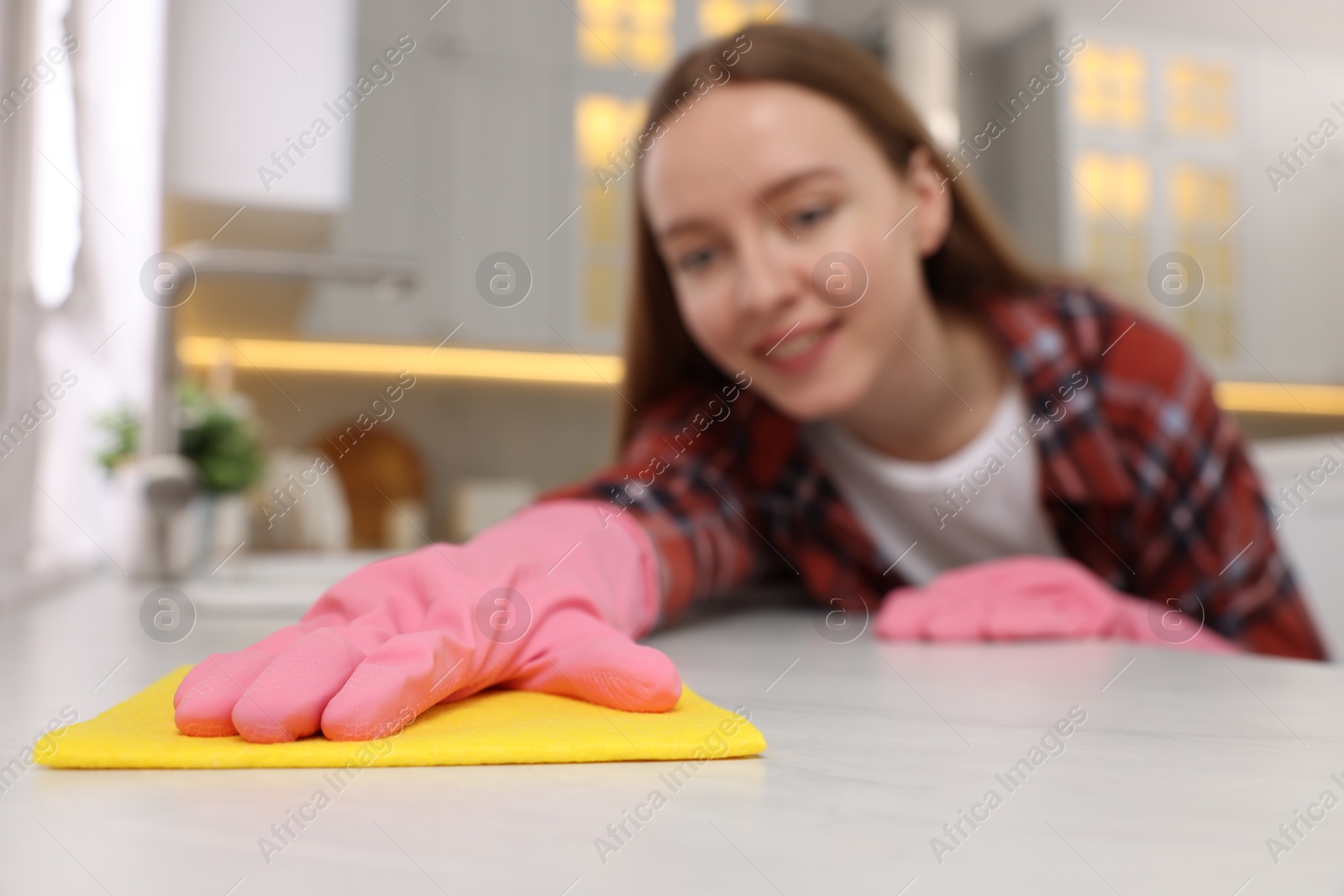 Photo of Woman cleaning white marble table with microfiber cloth in kitchen, selective focus