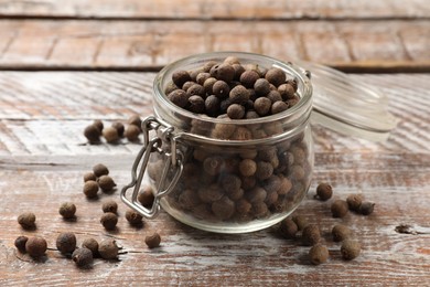 Photo of Aromatic allspice pepper grains in glass jar on wooden table