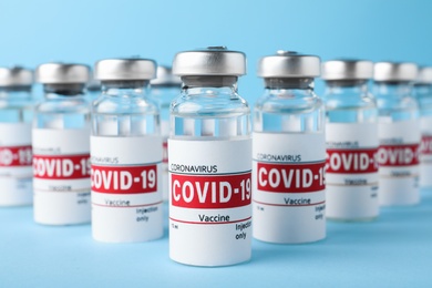 Photo of Glass vials with COVID-19 vaccine on light blue background