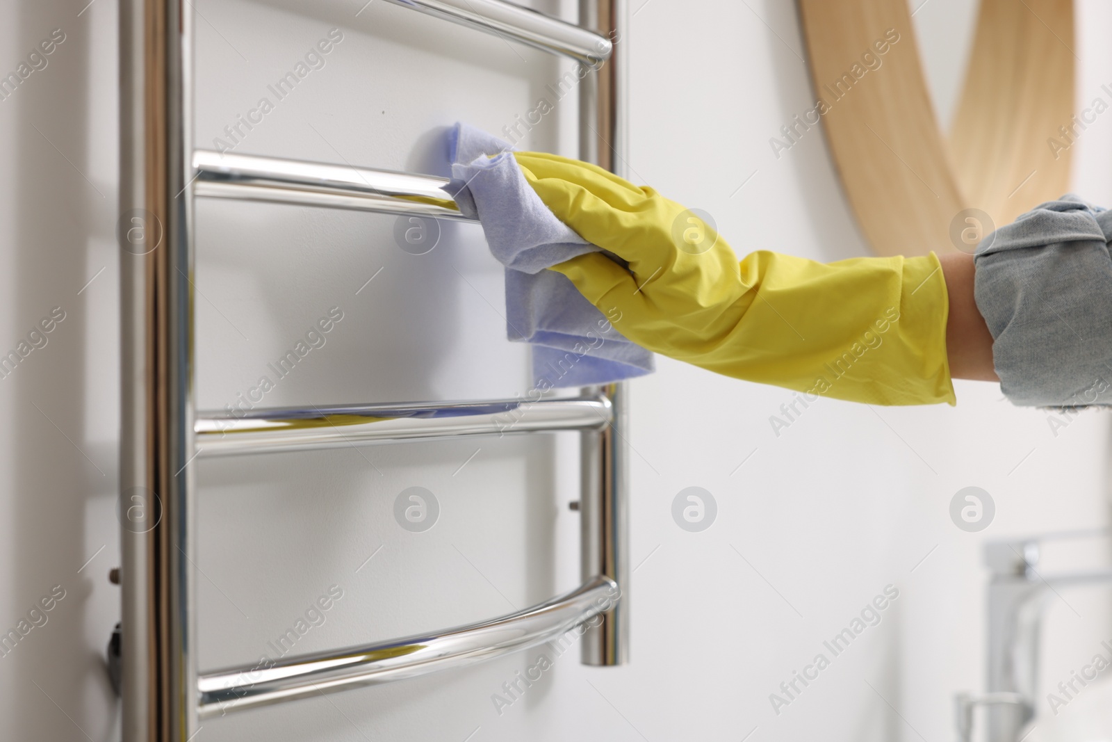 Photo of Woman cleaning heated towel rail with rag indoors, closeup