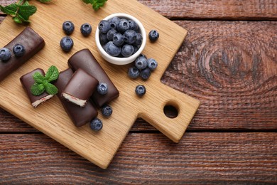 Photo of Delicious glazed curd snacks with fresh blueberries and mint on wooden table, top view. Space for text