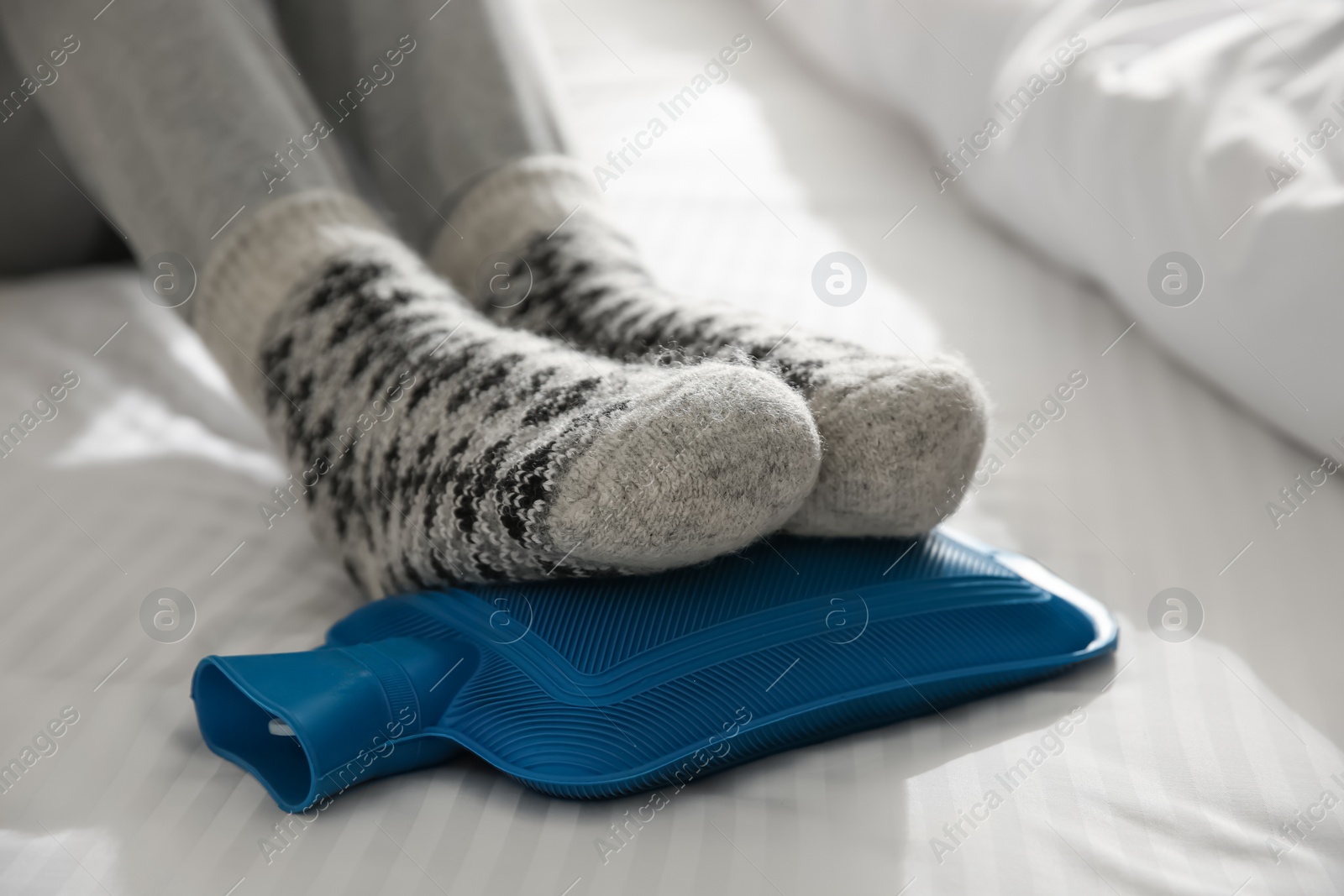 Photo of Person warming feet with hot water bottle on bed, closeup