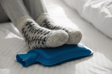 Person warming feet with hot water bottle on bed, closeup