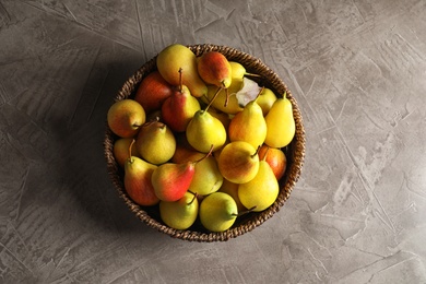 Wicker bowl with ripe pears on grey background, top view. Space for text