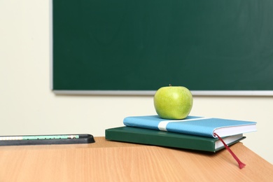 Photo of Wooden school desk with stationery and apple near chalkboard in classroom