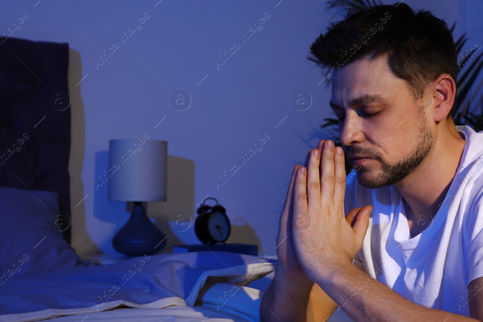 Photo of Handsome man saying bedtime prayer in dark room at night. Space for text