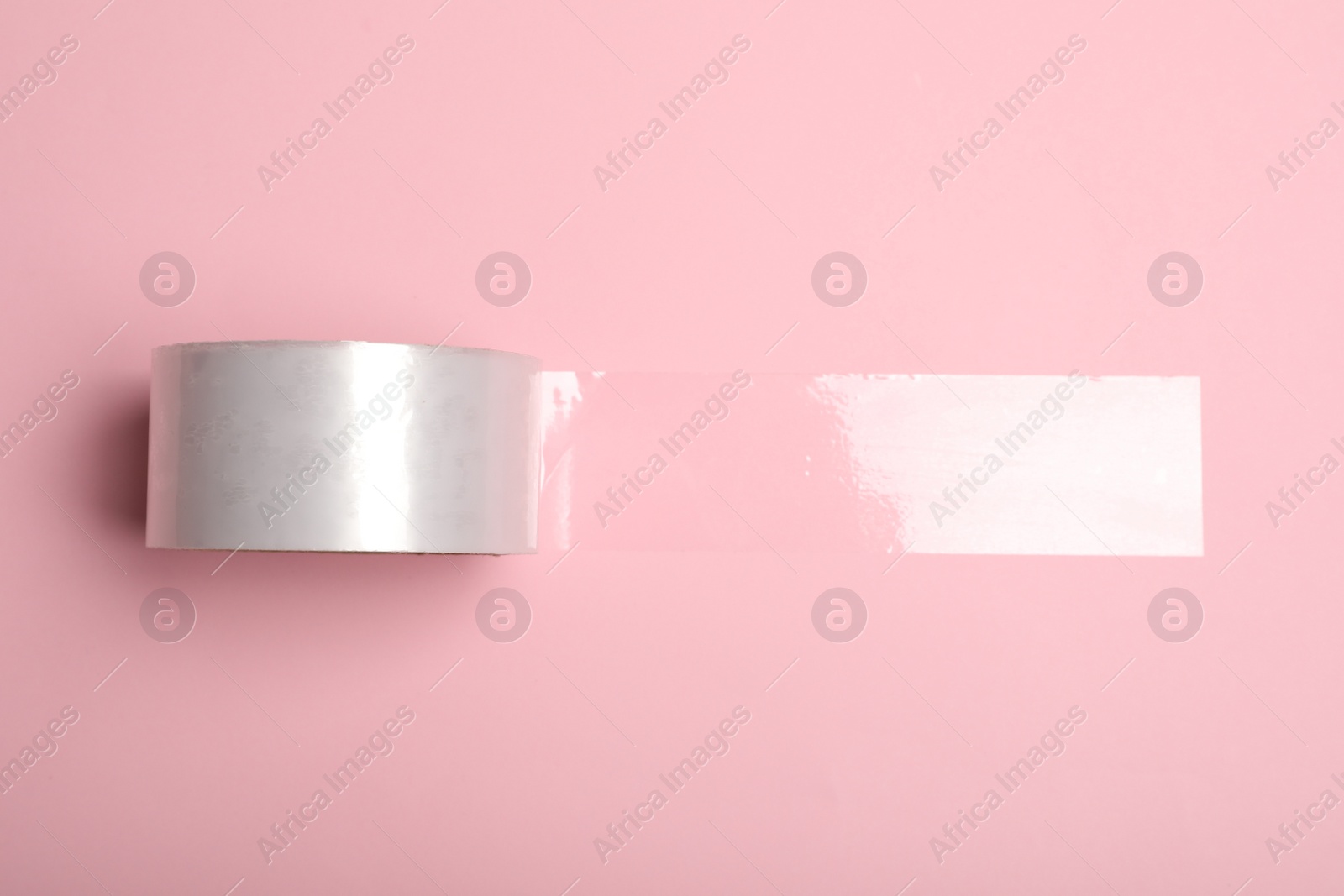 Photo of Roll of adhesive tape on pink background, top view