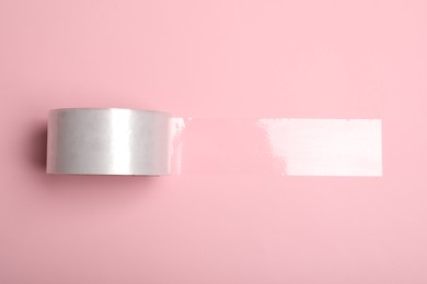 Roll of adhesive tape on pink background, top view