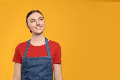 Photo of Beautiful young woman in clean denim apron on orange background. Space for text
