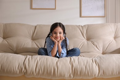 Little girl with headphones sitting on sofa at home