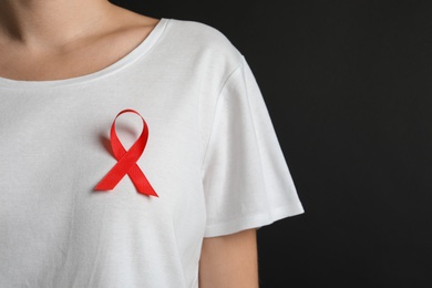 Photo of Woman with red ribbon on t-shirt against black background. Cancer awareness