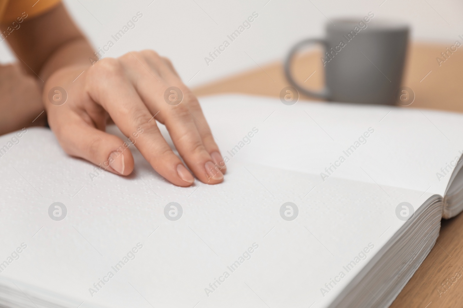 Photo of Blind woman reading book written in Braille at table, closeup