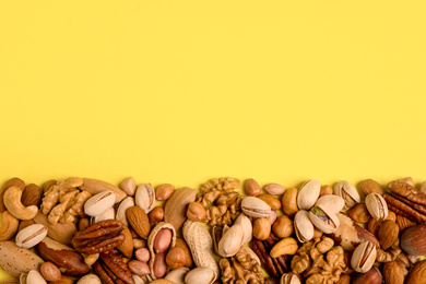 Photo of Different delicious nuts on yellow background, flat lay. Space for text