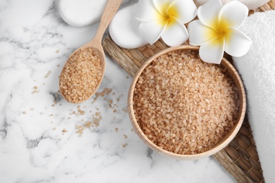 Salt for spa scrubbing procedure and flowers on white marble background, flat lay