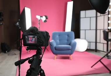 Photo of Stylish blue armchair in photo studio with professional equipment, focus on camera