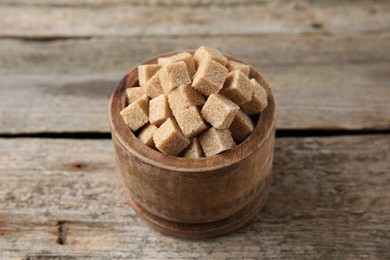 Photo of Brown sugar cubes in bowl on wooden table, closeup