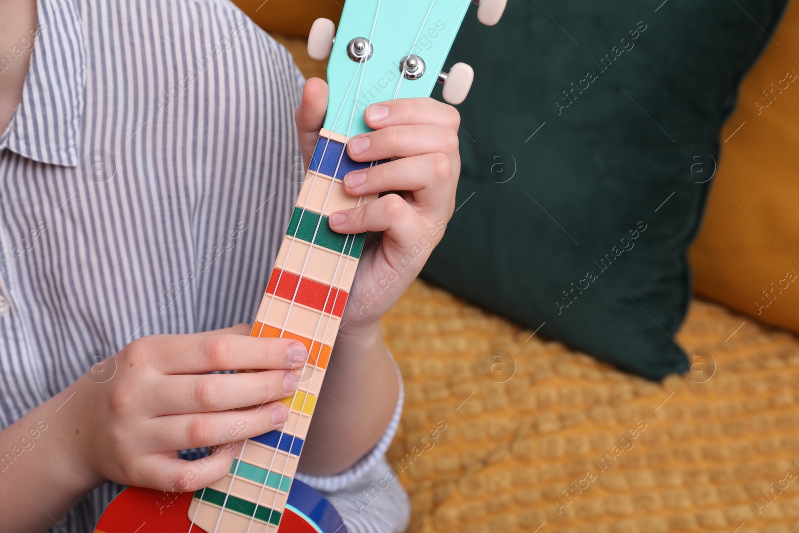 Photo of Woman playing ukulele on sofa at home, closeup