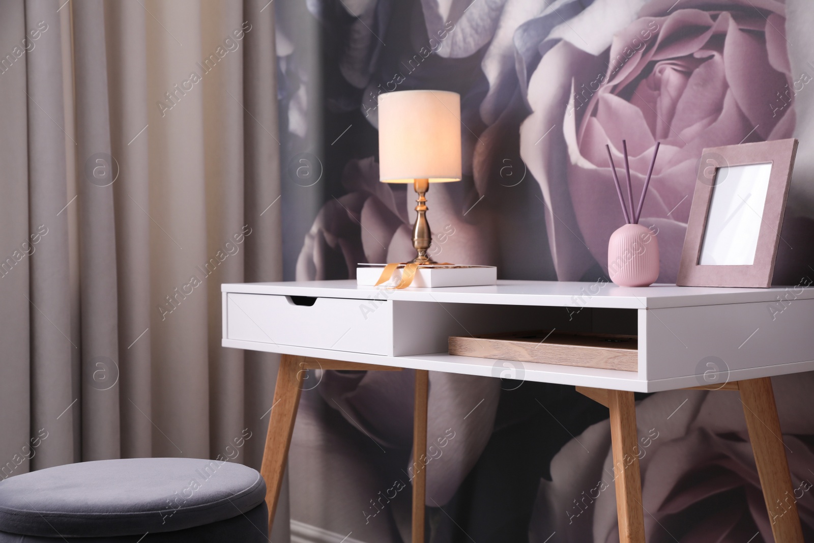 Photo of Lamp, frame and air freshener on table near wall with floral pattern. Stylish room interior