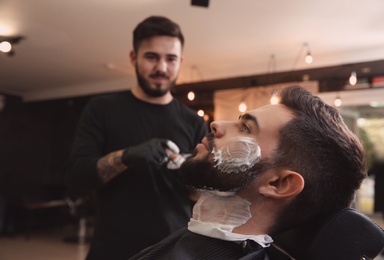 Young man with shaving foam on face in barbershop. Professional service