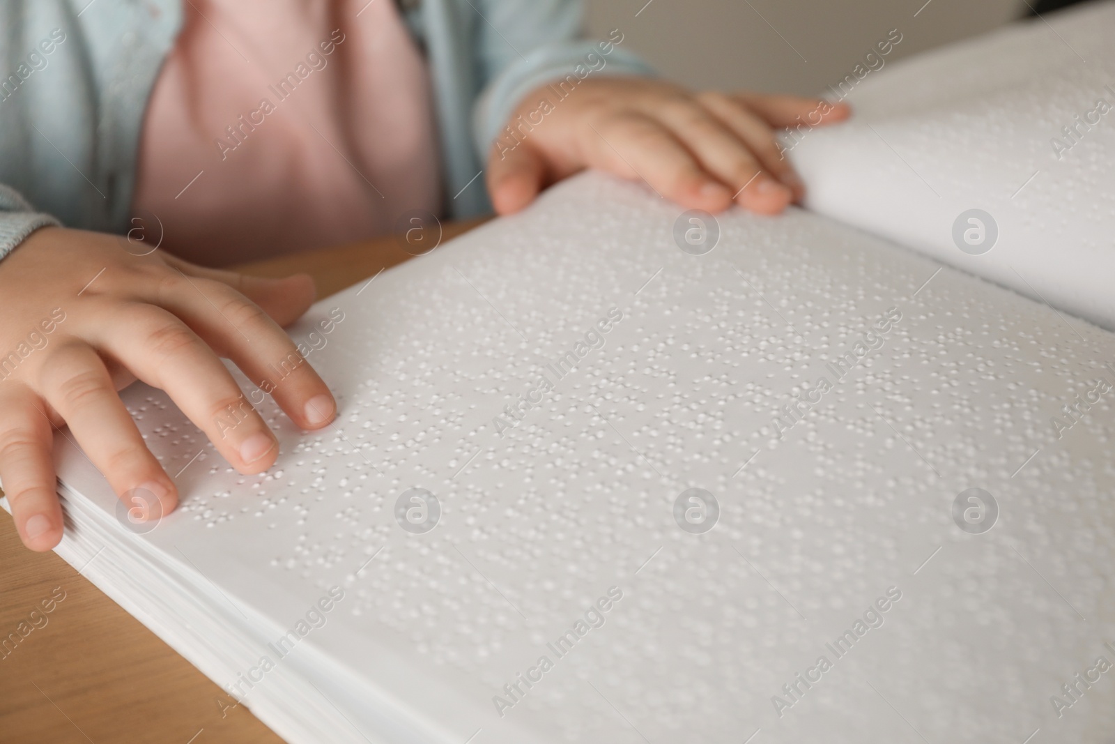 Photo of Blind child reading book written in Braille at table, closeup