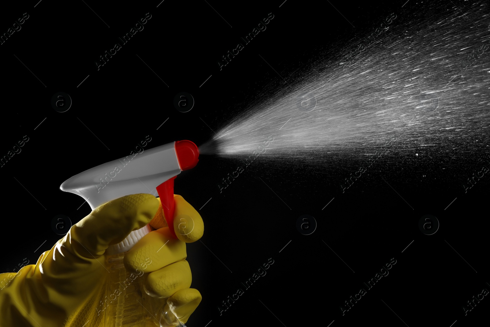 Photo of Woman spraying liquid from bottle on black background, closeup