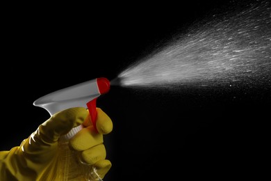 Photo of Woman spraying liquid from bottle on black background, closeup