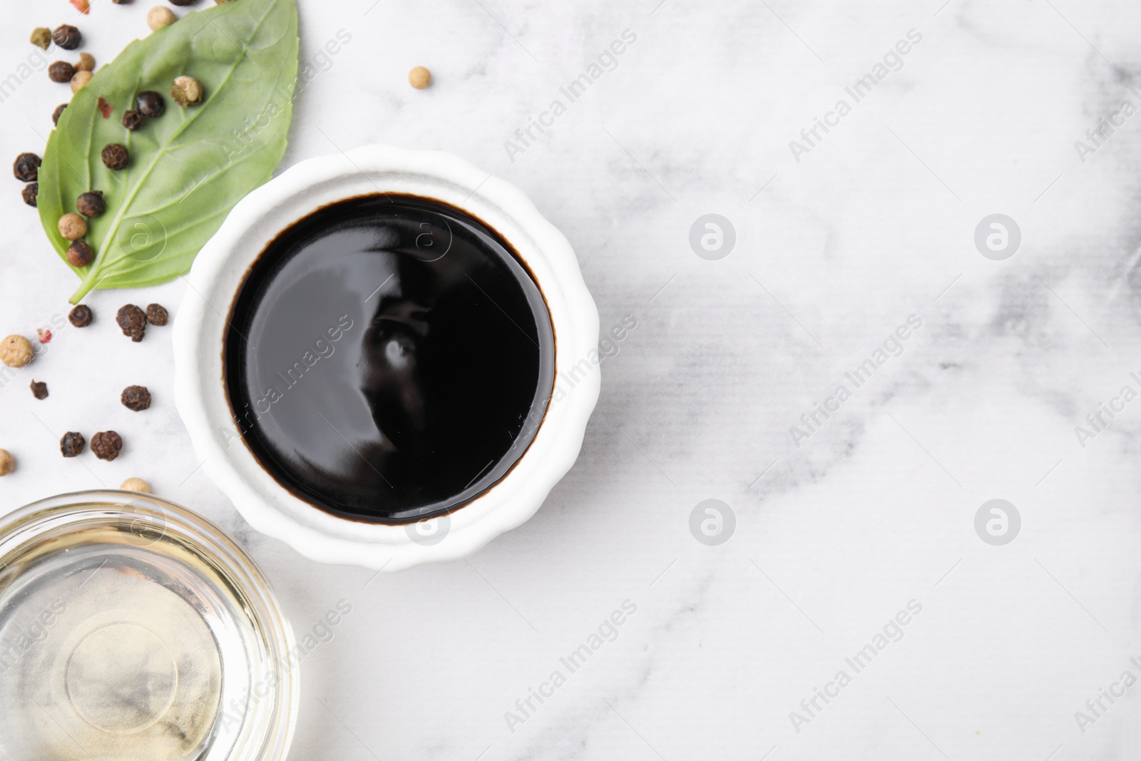 Photo of Bowl with balsamic vinegar and ingredients on white marble table, flat lay. Space for text