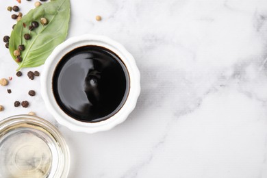 Bowl with balsamic vinegar and ingredients on white marble table, flat lay. Space for text