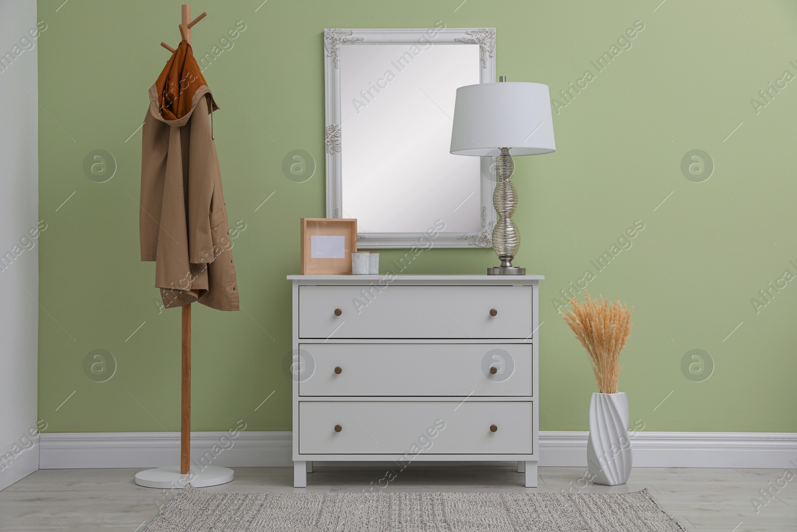 Photo of White chest of drawers with decor, coat stand and mirror in hallway. Interior design