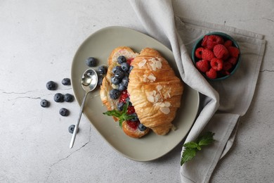 Delicious croissant with berries, almond flakes and spoon on light grey table, flat lay