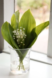 Photo of Beautiful lily of the valley flowers in glass vase on window sill indoors