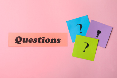 Photo of Word QUESTIONS and query marks on pink background, flat lay
