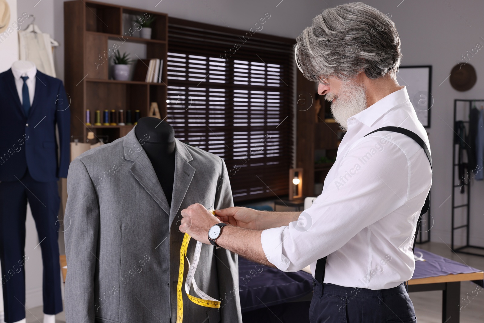 Photo of Professional tailor with measuring tape working in atelier