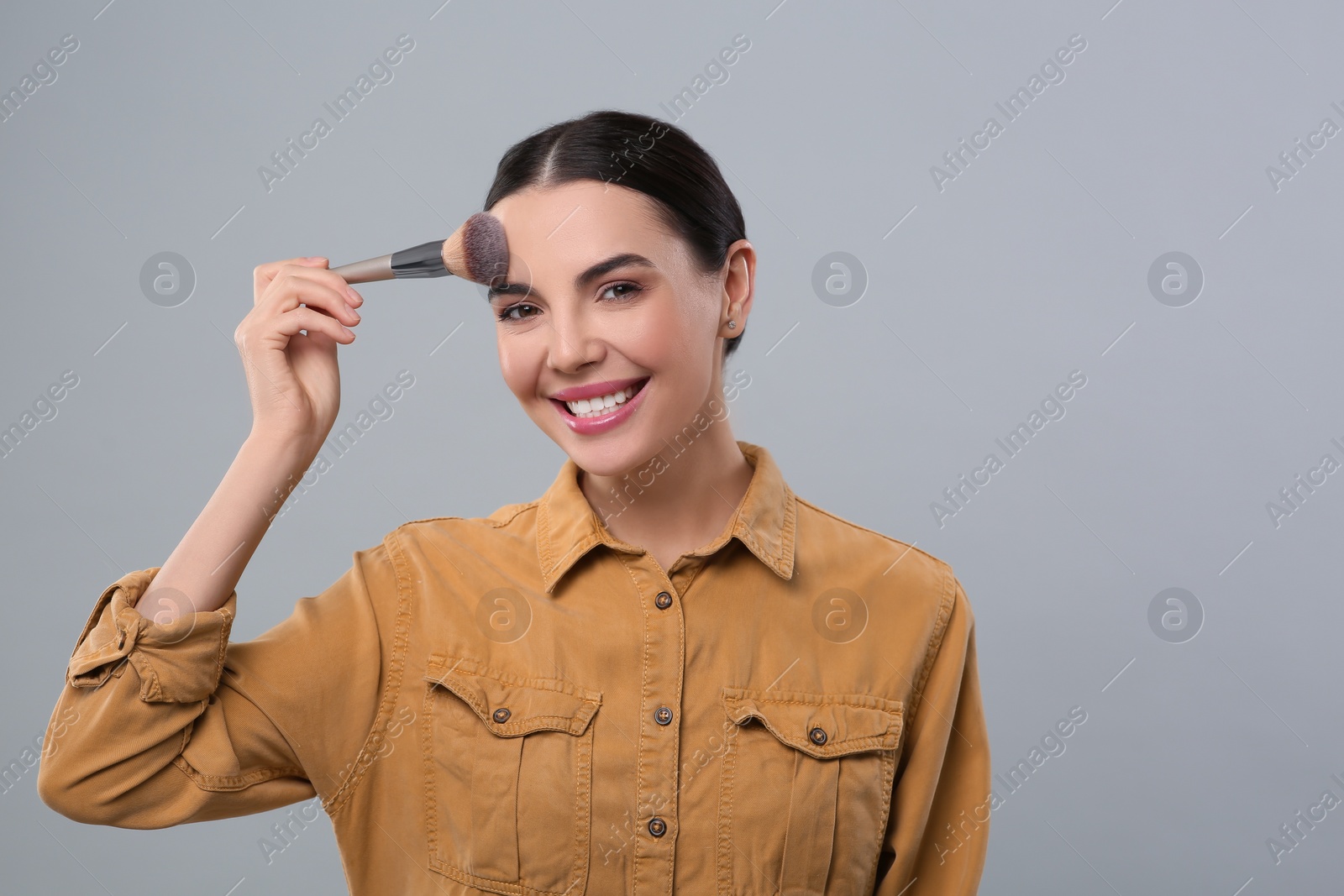 Photo of Happy woman applying makeup on light grey background, space for text