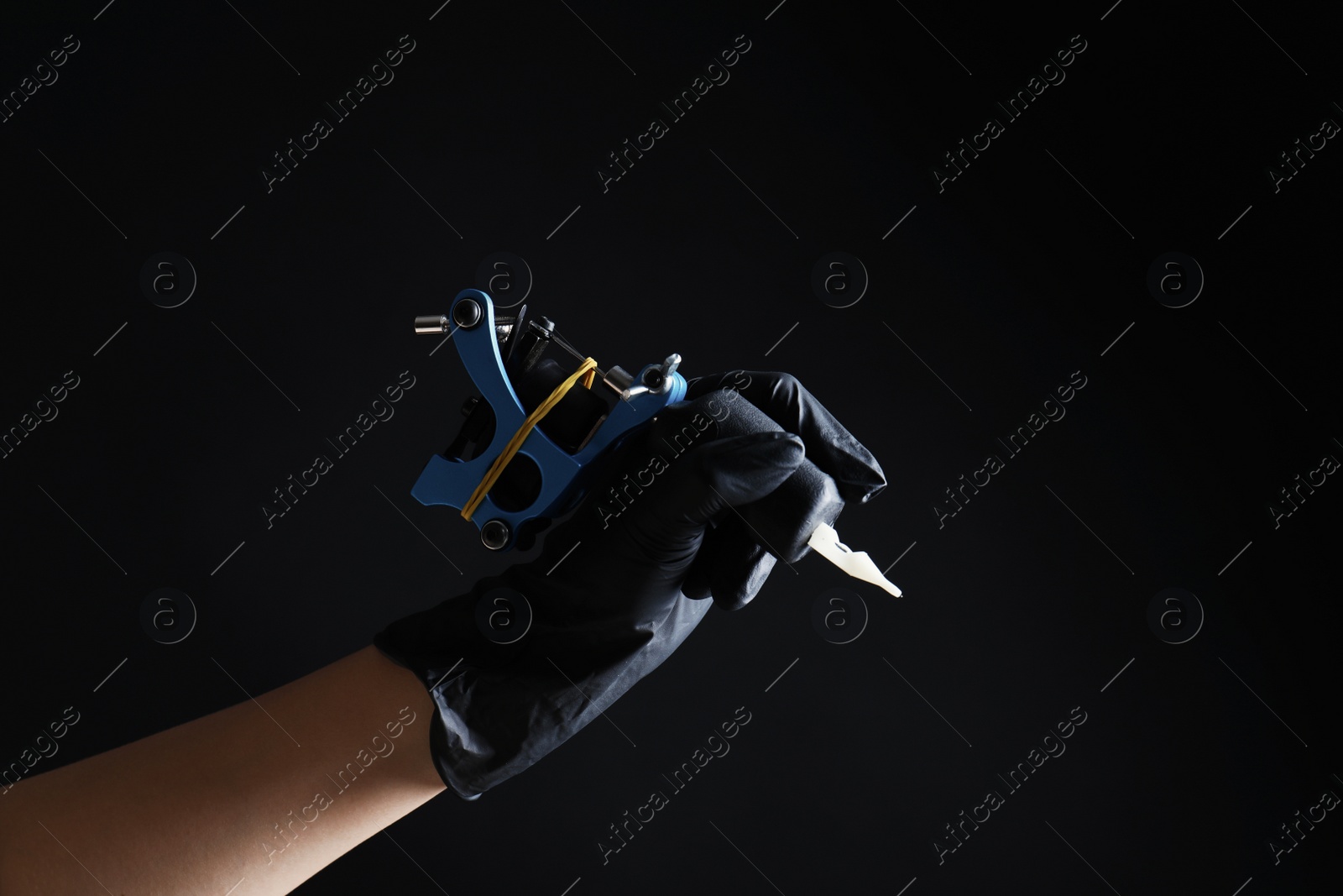 Photo of Professional tattoo artist with machine on black background, closeup. Space for text