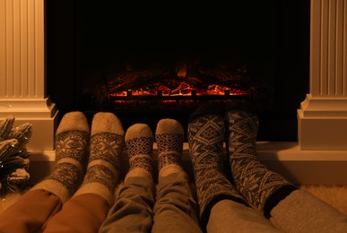 Photo of Lovely family in warm socks resting near fireplace at home, closeup