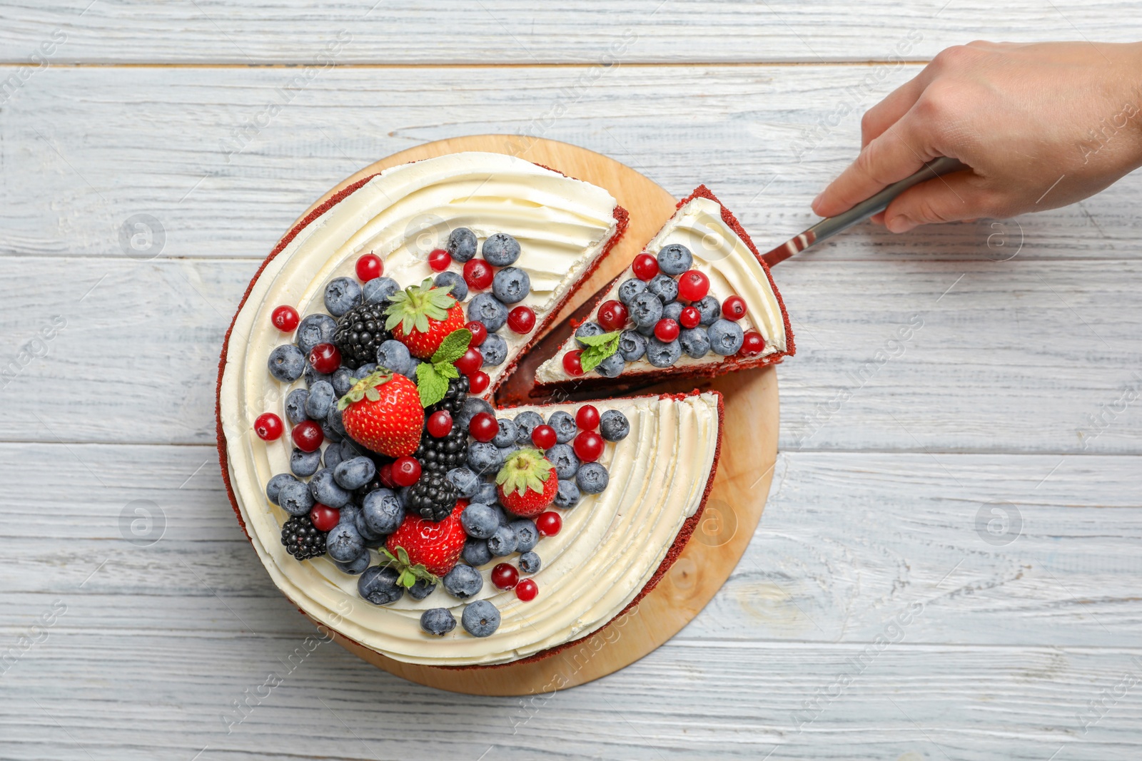 Photo of Woman taking piece of delicious homemade red velvet cake from table, top view