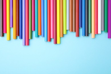 Colorful wooden pencils on light blue background, flat lay. Space for text