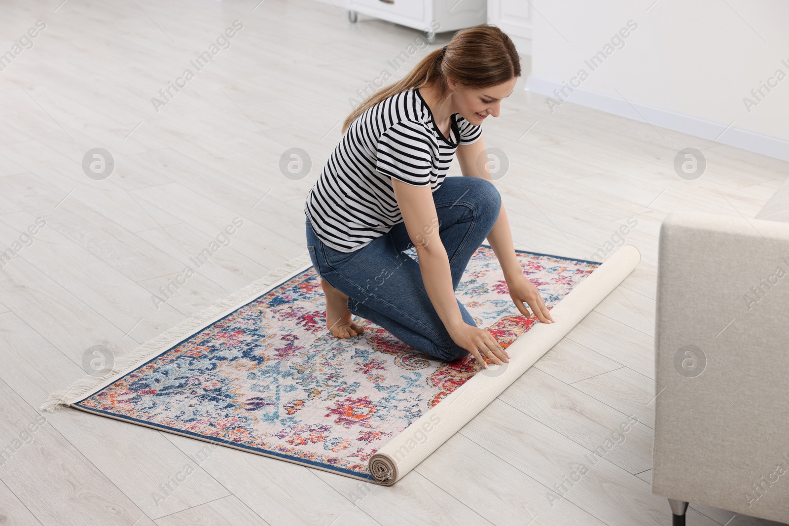 Photo of Smiling woman unrolling carpet with beautiful pattern on floor in room