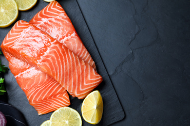 Photo of Top view of fresh raw salmon with lemon on black table, space for text. Fish delicacy
