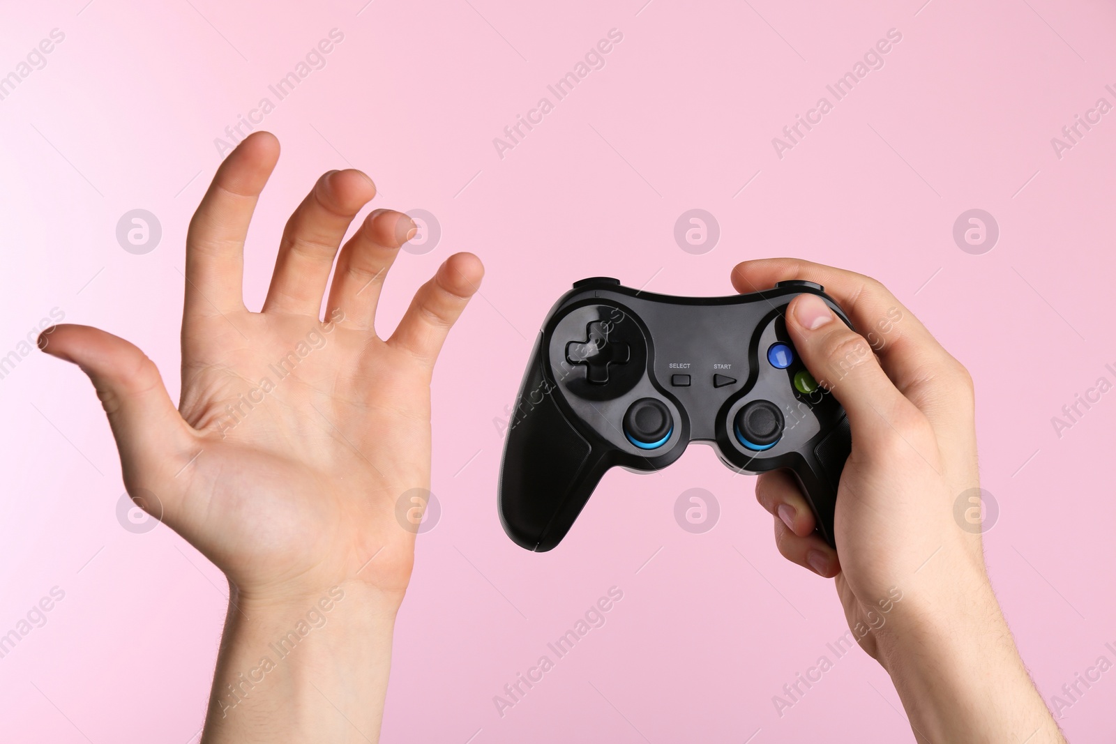 Photo of Man using wireless game controller on pink background, closeup