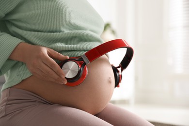 Photo of Pregnant woman with headphones on her belly indoors, closeup