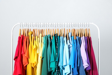 Photo of Rack with bright clothes on light blue background. Rainbow colors