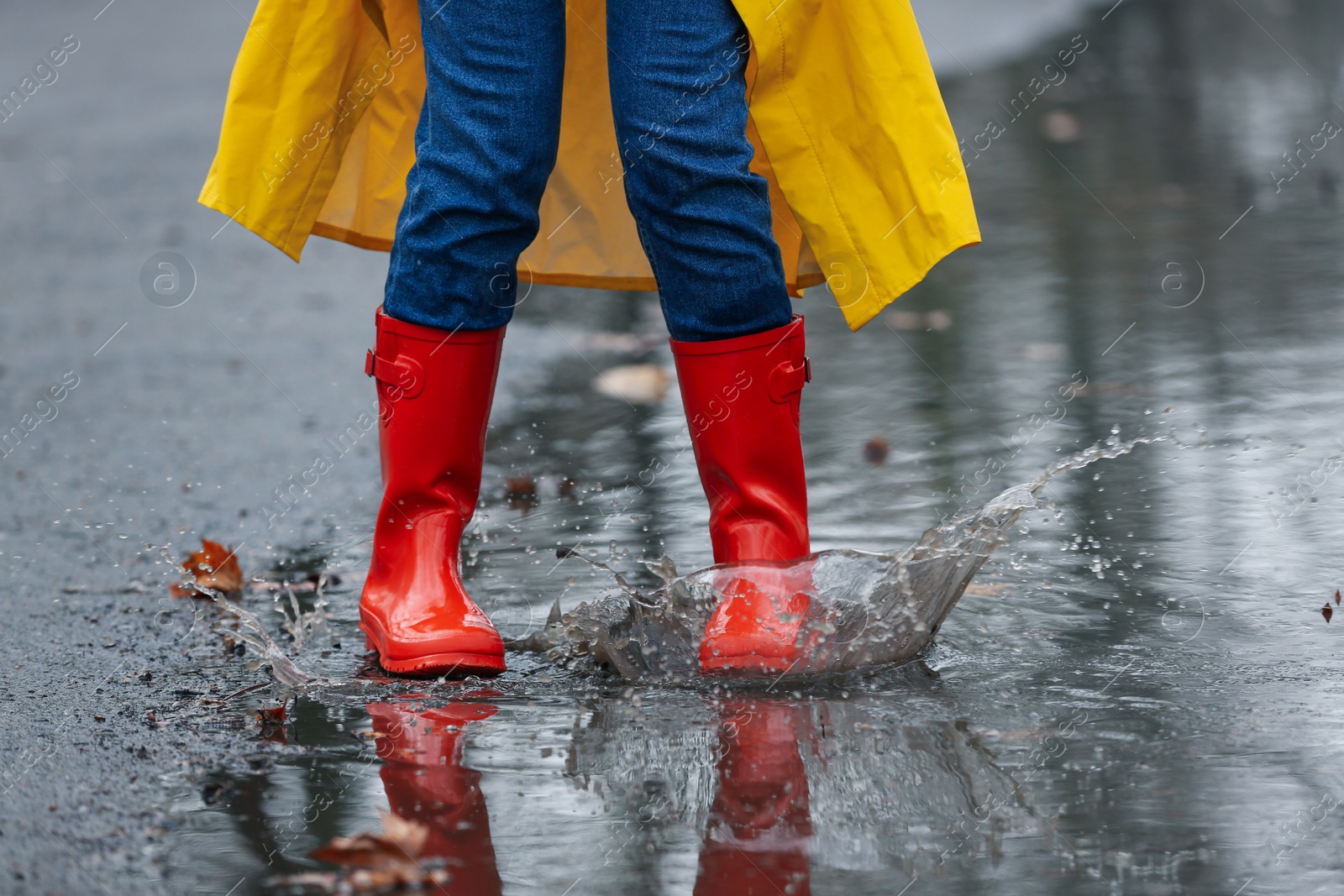 Photo of Woman splashing in puddle outdoors on rainy day, closeup