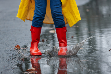 Photo of Woman splashing in puddle outdoors on rainy day, closeup