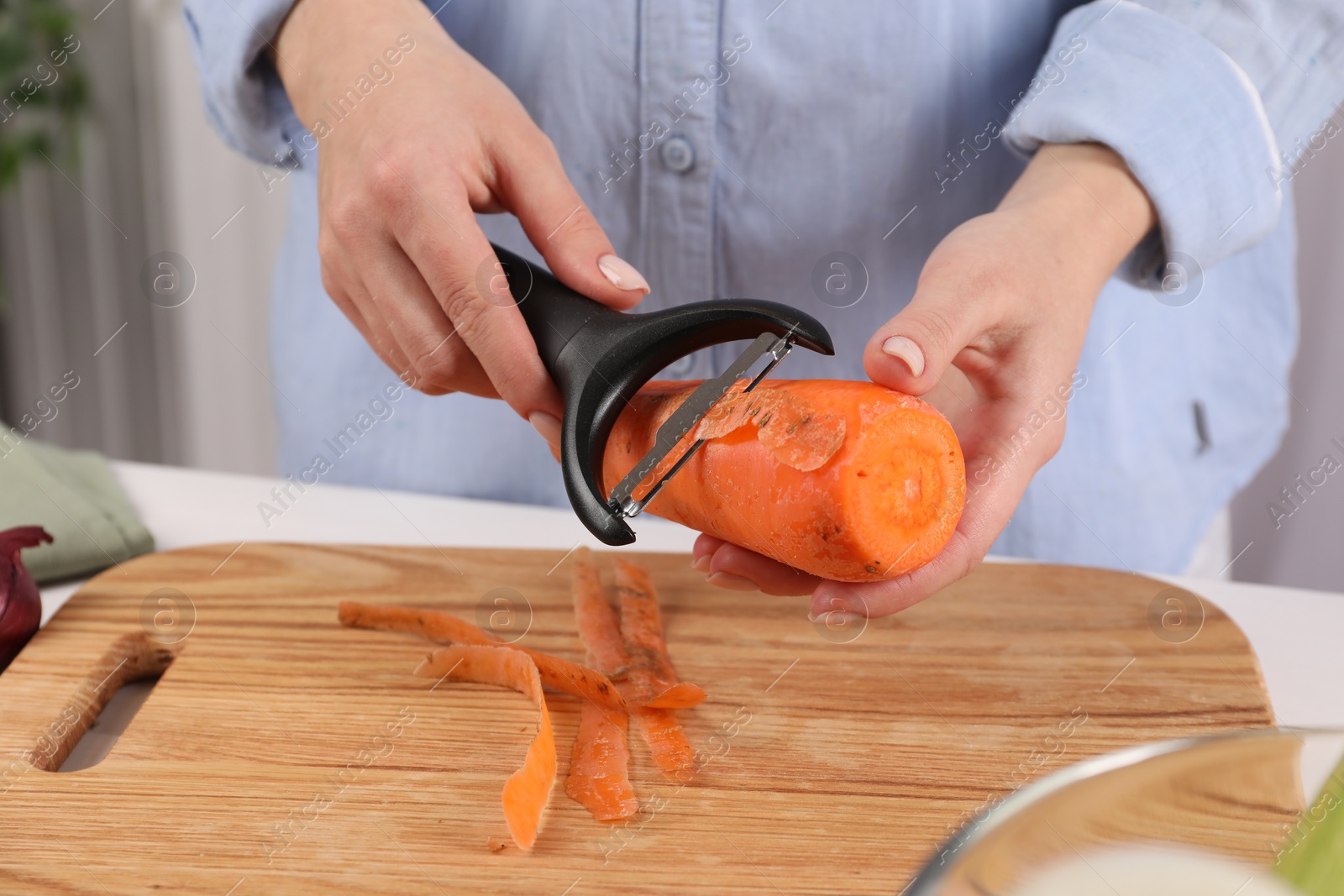 Photo of Woman peeling fresh carrot at table indoors, closeup