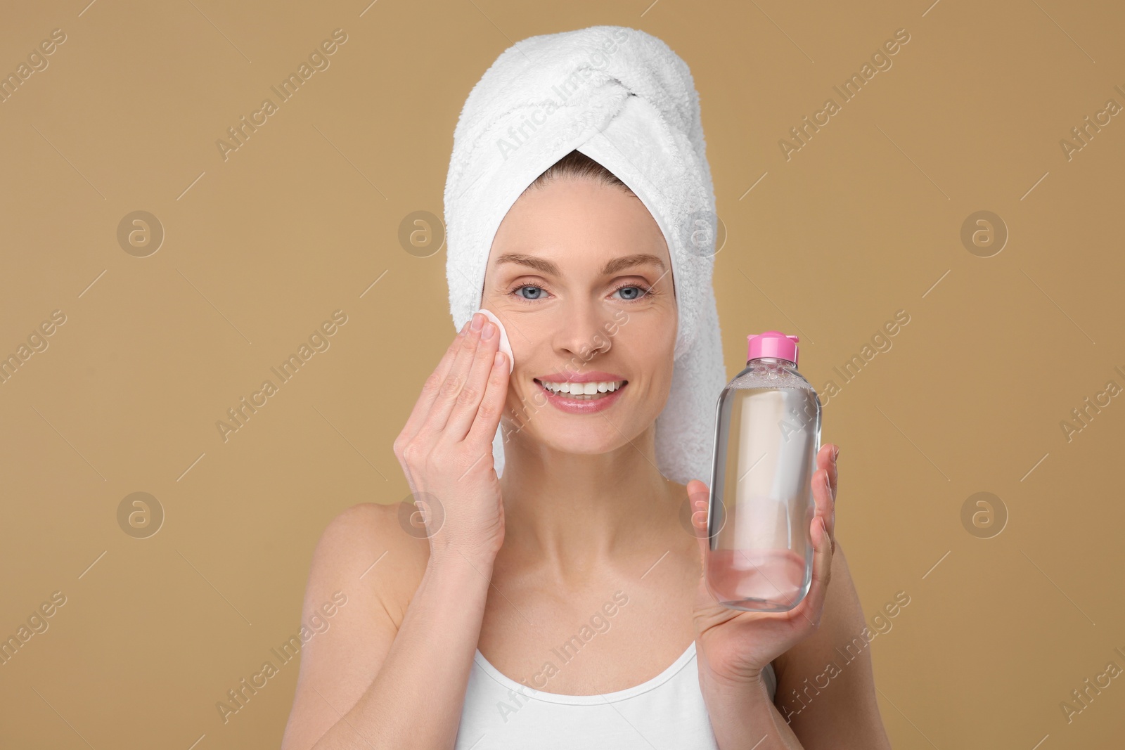 Photo of Beautiful woman in terry towel removing makeup with cotton pad on beige background