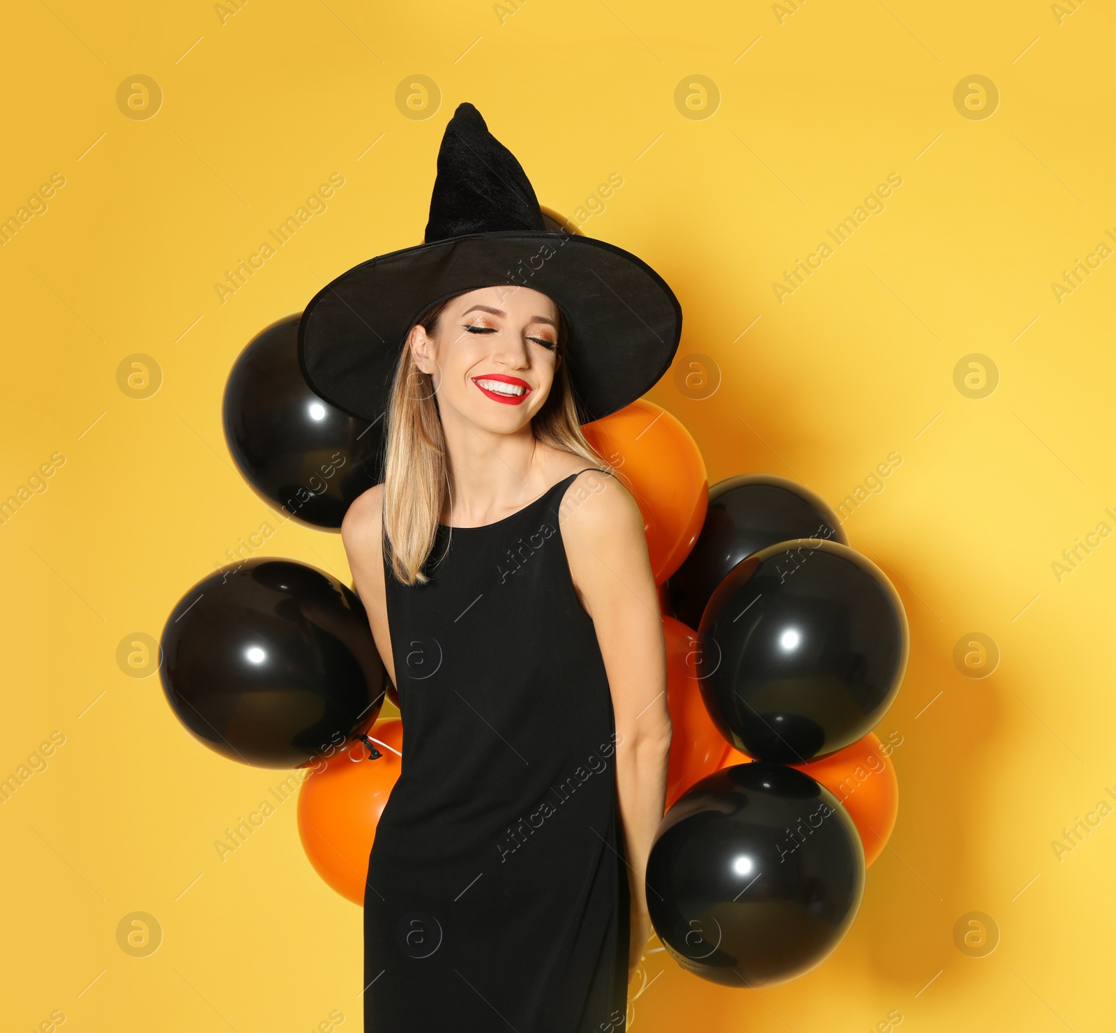 Photo of Beautiful woman wearing witch costume with balloons for Halloween party on yellow background, space for text