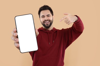 Happy man holding smartphone with empty screen on beige background