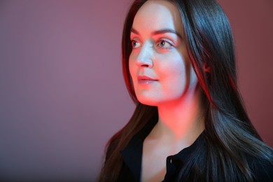 Photo of Portrait of beautiful young woman on color background with neon lights. Space for text